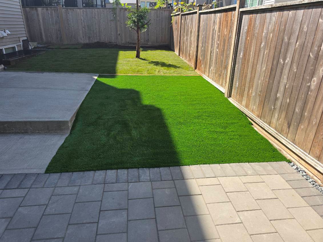 Backyard with new artificial turf lawn and grey paver patio along a cedar fence
